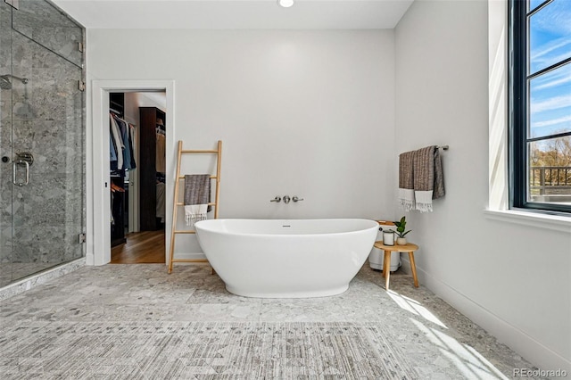 full bath with a stall shower, a soaking tub, a spacious closet, and baseboards