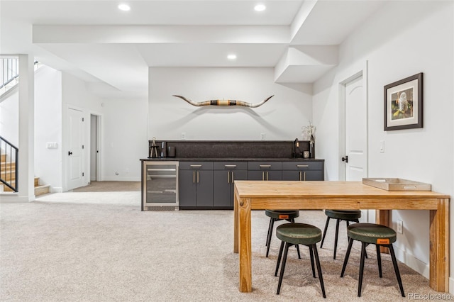 kitchen with wine cooler, light colored carpet, recessed lighting, dark countertops, and baseboards