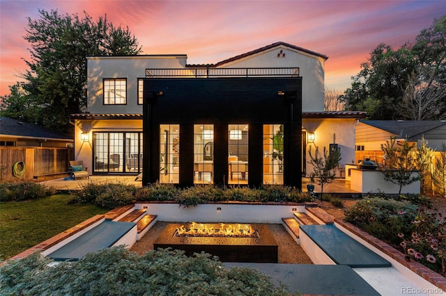 back of house at dusk featuring a fire pit, stucco siding, and a tiled roof