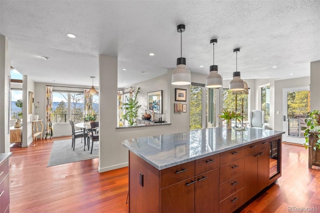 12653 Rancho Ct, Conifer, CO 80433 - kitchen with a textured ceiling, wood finished floors, light stone countertops, a center island, and hanging light fixtures