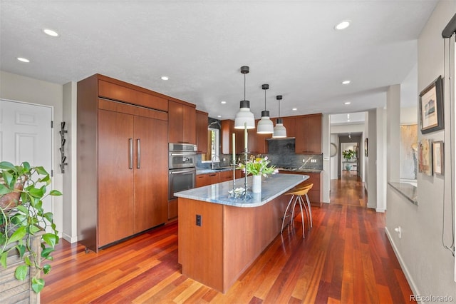 12653 Rancho Ct, Conifer, CO 80433 - kitchen with stainless steel double oven, a kitchen island, a kitchen bar, dark wood finished floors, and recessed lighting