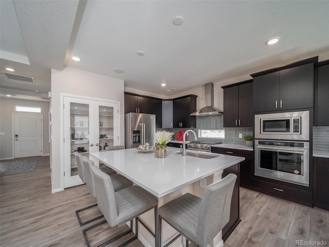 kitchen featuring a kitchen bar, appliances with stainless steel finishes, sink, wall chimney range hood, and an island with sink