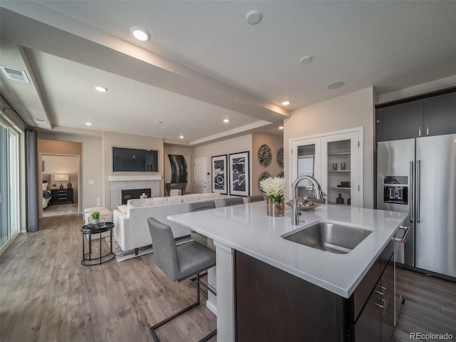 kitchen with a kitchen breakfast bar, high end fridge, sink, a tile fireplace, and a center island with sink