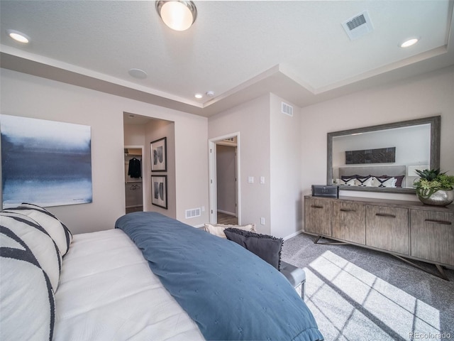 bedroom featuring a walk in closet, light colored carpet, and a tray ceiling