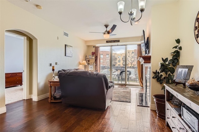 living area with baseboards, visible vents, ceiling fan with notable chandelier, dark wood-type flooring, and arched walkways