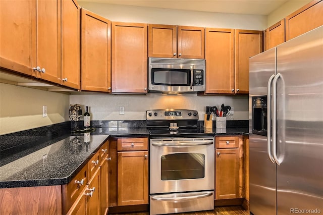 kitchen with stainless steel appliances, brown cabinetry, and dark stone countertops
