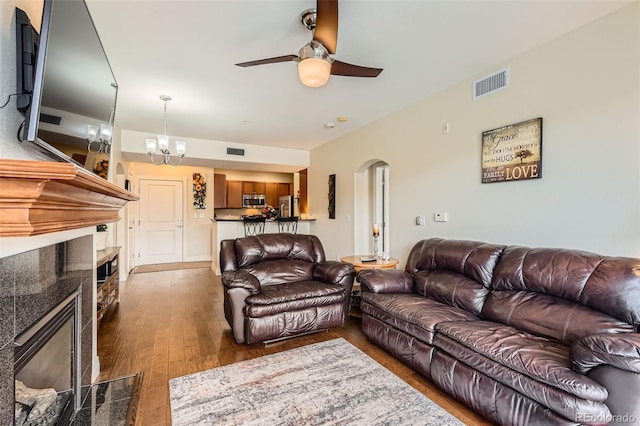 living area featuring a tile fireplace, a ceiling fan, arched walkways, wood finished floors, and a chandelier