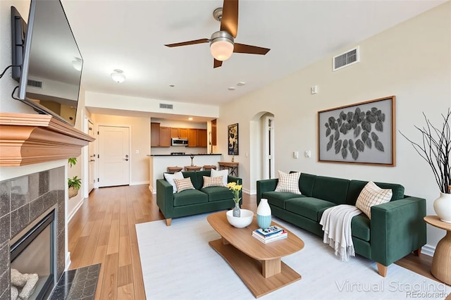 9019 E Panorama Cir Unit D207, Englewood, CO 80112 - living room featuring a tiled fireplace, arched walkways, a ceiling fan, light wood-style floors, and baseboards