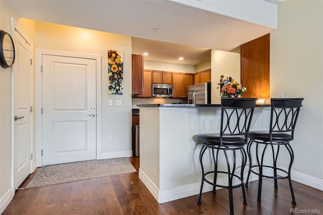9019 E Panorama Cir Unit D207, Englewood, CO 80112 - kitchen featuring appliances with stainless steel finishes, brown cabinets, dark wood-type flooring, a kitchen bar, and a peninsula