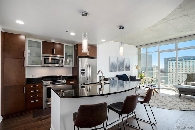 kitchen with stainless steel appliances, a sink, dark wood-style flooring, a kitchen bar, and dark countertops