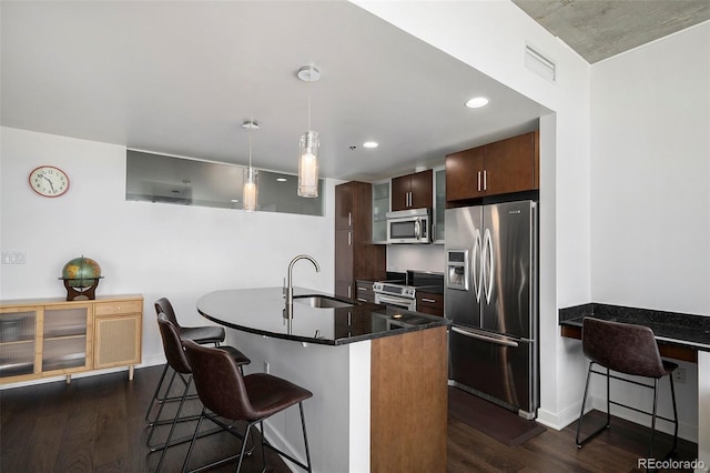 kitchen featuring appliances with stainless steel finishes, a sink, dark wood-style floors, a kitchen bar, and hanging light fixtures