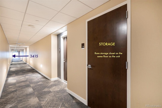 hallway with carpet floors, baseboards, and a paneled ceiling