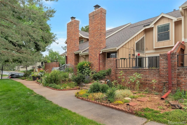 11894 Elk Head Range Rd, Littleton, CO 80127 - view of home's exterior with a chimney, roof with shingles, board and batten siding, brick siding, and a lawn