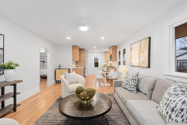 living room featuring arched walkways, recessed lighting, light wood-type flooring, and baseboards