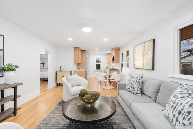 living area with recessed lighting, baseboards, arched walkways, and light wood finished floors