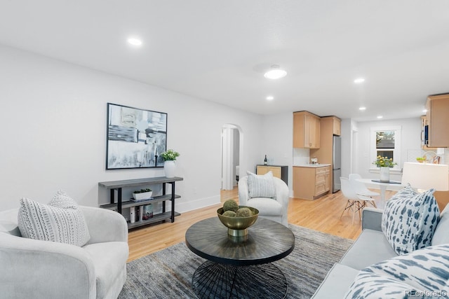 living area with recessed lighting, light wood-style floors, arched walkways, and baseboards