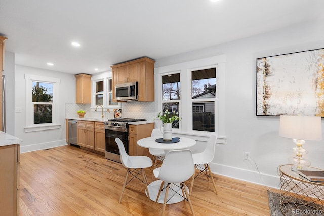 kitchen featuring light wood-style flooring, a sink, stainless steel appliances, light countertops, and tasteful backsplash