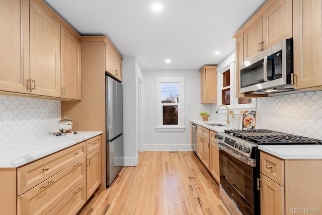 kitchen featuring baseboards, light wood finished floors, light brown cabinetry, a sink, and appliances with stainless steel finishes