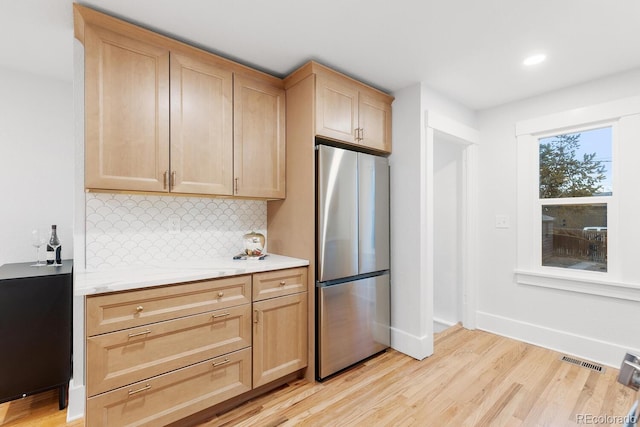 kitchen with light wood finished floors, visible vents, light brown cabinets, decorative backsplash, and freestanding refrigerator