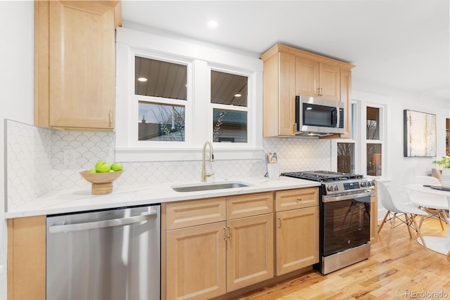 kitchen featuring light brown cabinets, appliances with stainless steel finishes, light wood-style floors, and a sink