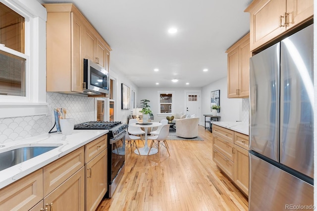 kitchen featuring light brown cabinetry, stainless steel appliances, light wood-style floors, open floor plan, and backsplash