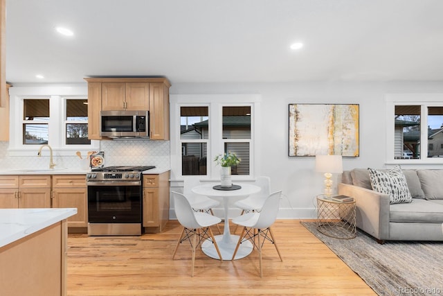 kitchen featuring light wood-type flooring, a sink, appliances with stainless steel finishes, open floor plan, and backsplash