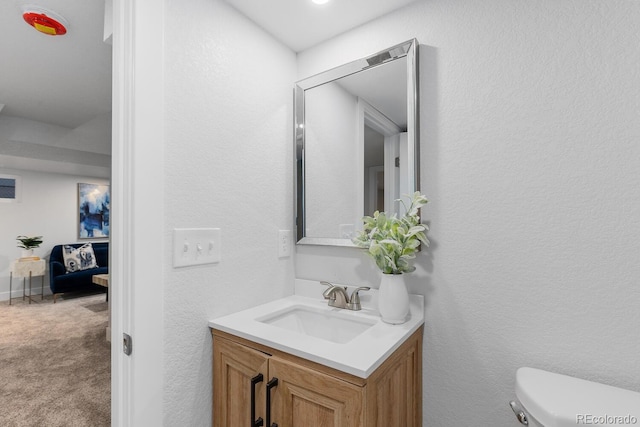 bathroom with toilet, vanity, and a textured wall