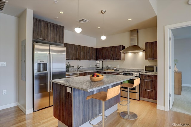 kitchen with dark brown cabinetry, visible vents, wall chimney exhaust hood, appliances with stainless steel finishes, and a sink