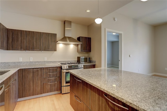 kitchen featuring decorative light fixtures, stainless steel appliances, light wood-style flooring, modern cabinets, and wall chimney exhaust hood