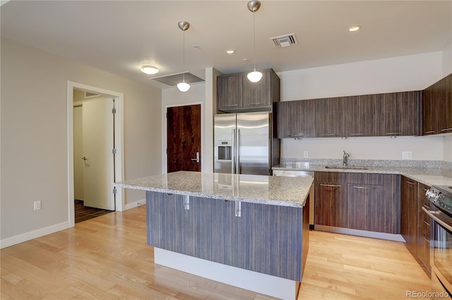 kitchen with high end refrigerator, a kitchen island, a sink, visible vents, and electric stove