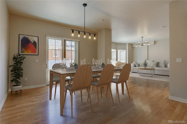 dining space with light wood-type flooring, baseboards, and a notable chandelier