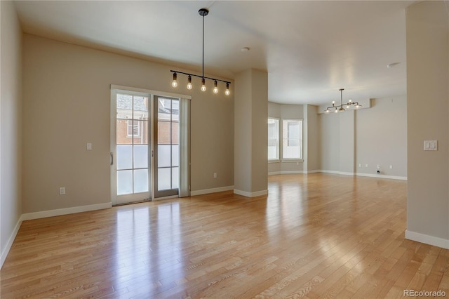 spare room with light wood finished floors, baseboards, and a notable chandelier