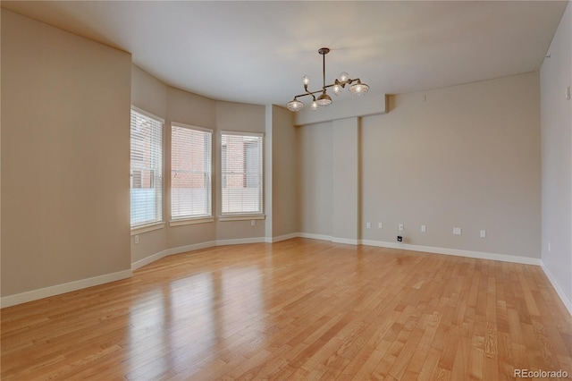 spare room featuring a chandelier, light wood finished floors, and baseboards