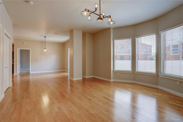 spare room featuring light wood-type flooring, baseboards, and a notable chandelier