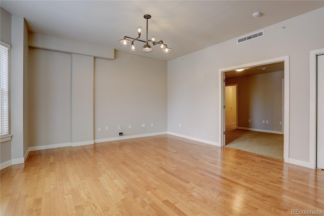 spare room with visible vents, an inviting chandelier, light wood-type flooring, plenty of natural light, and baseboards