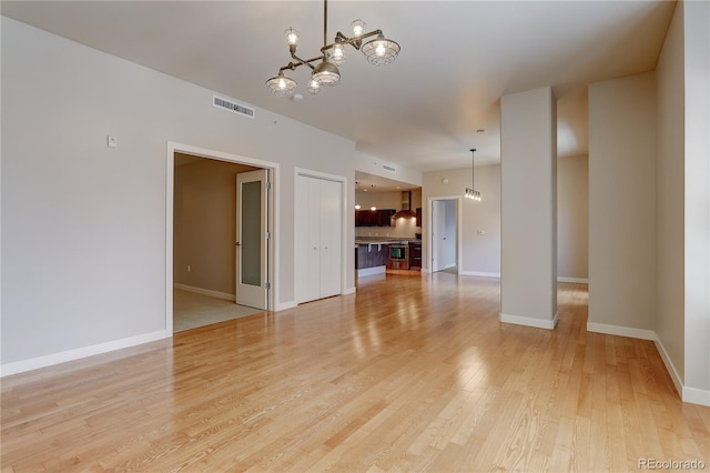 unfurnished room featuring light wood finished floors, an inviting chandelier, visible vents, and baseboards