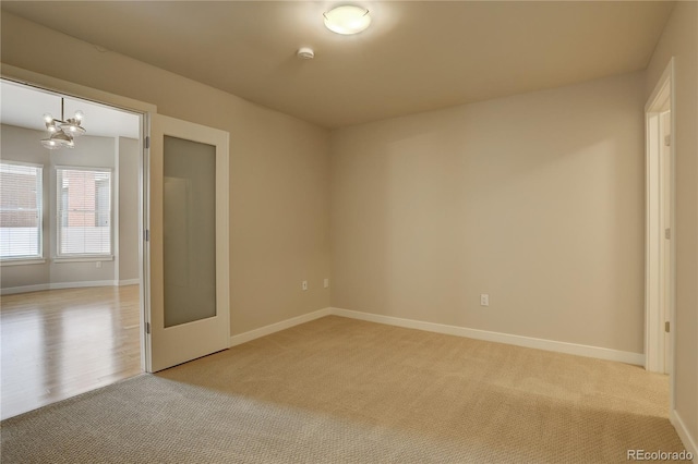 unfurnished room featuring light carpet, baseboards, and a chandelier