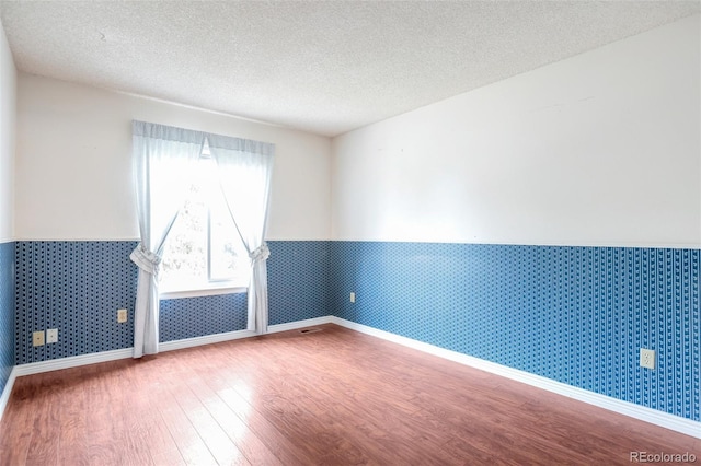 19421 E Milan Cir, Aurora, CO 80013 - unfurnished room with wood finished floors, wainscoting, a textured ceiling, wallpapered walls, and baseboards