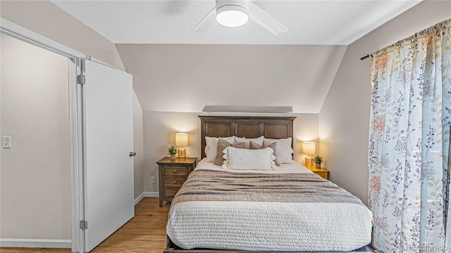 bedroom featuring light hardwood / wood-style floors, vaulted ceiling, a textured ceiling, and ceiling fan