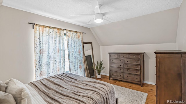 bedroom with a textured ceiling, lofted ceiling, light wood-type flooring, and ceiling fan