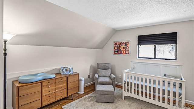 bedroom featuring a nursery area, a textured ceiling, lofted ceiling, and dark hardwood / wood-style flooring