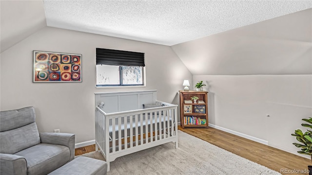 bedroom featuring lofted ceiling, a crib, wood-type flooring, and a textured ceiling