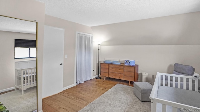 bedroom with a crib, a textured ceiling, light wood-type flooring, and vaulted ceiling