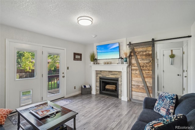 living room featuring hardwood / wood-style floors, a barn door, a textured ceiling, and a stone fireplace