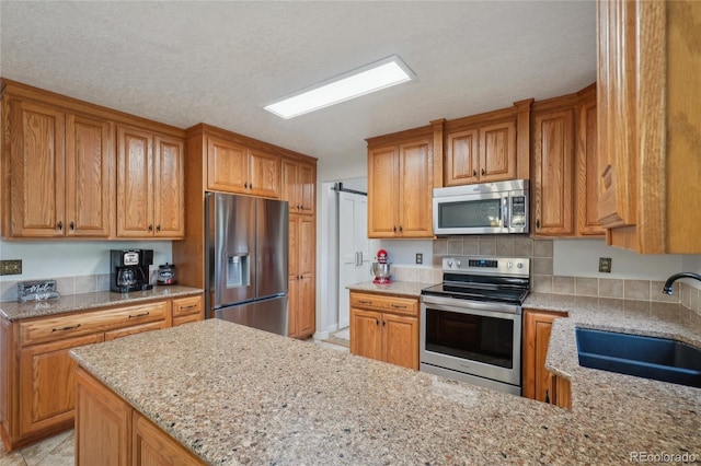 kitchen featuring light stone counters, sink, stainless steel appliances, and a textured ceiling