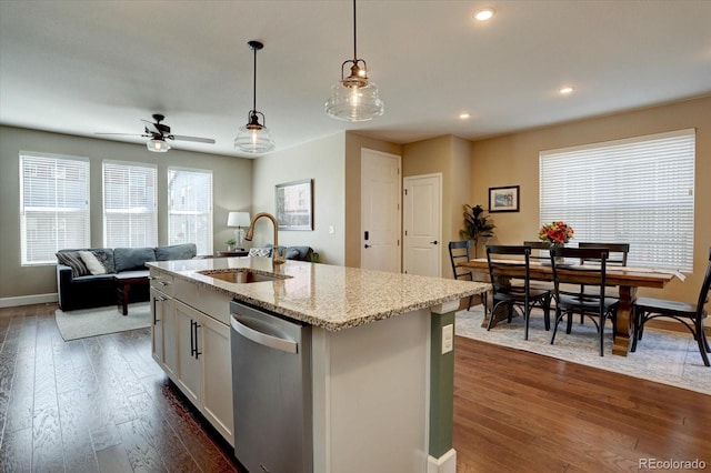 kitchen with light stone counters, a sink, stainless steel dishwasher, an island with sink, and pendant lighting