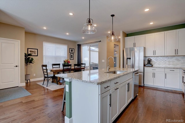 kitchen with light stone counters, a kitchen island with sink, a sink, white cabinetry, and decorative light fixtures