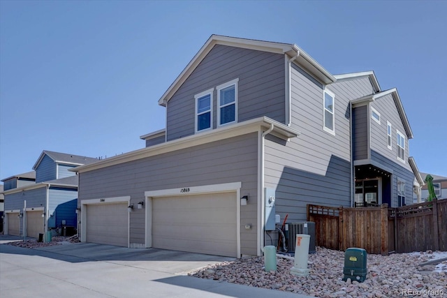 view of side of property featuring concrete driveway, an attached garage, cooling unit, and fence