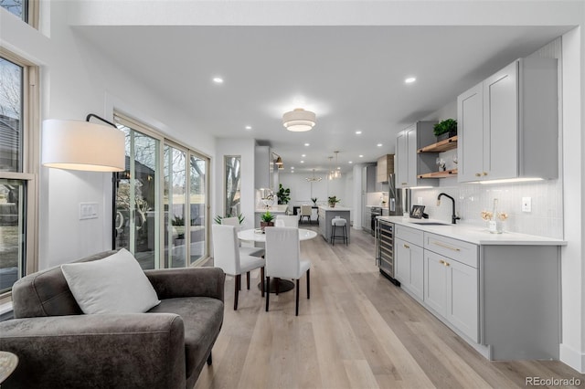 kitchen with sink, tasteful backsplash, light hardwood / wood-style flooring, beverage cooler, and white cabinets