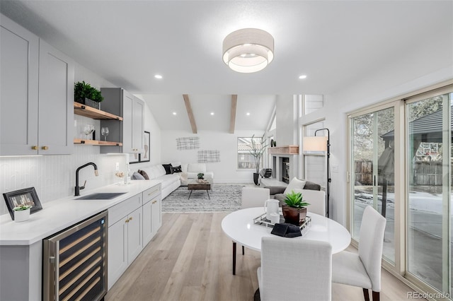 kitchen with wine cooler, sink, tasteful backsplash, lofted ceiling with beams, and light hardwood / wood-style flooring